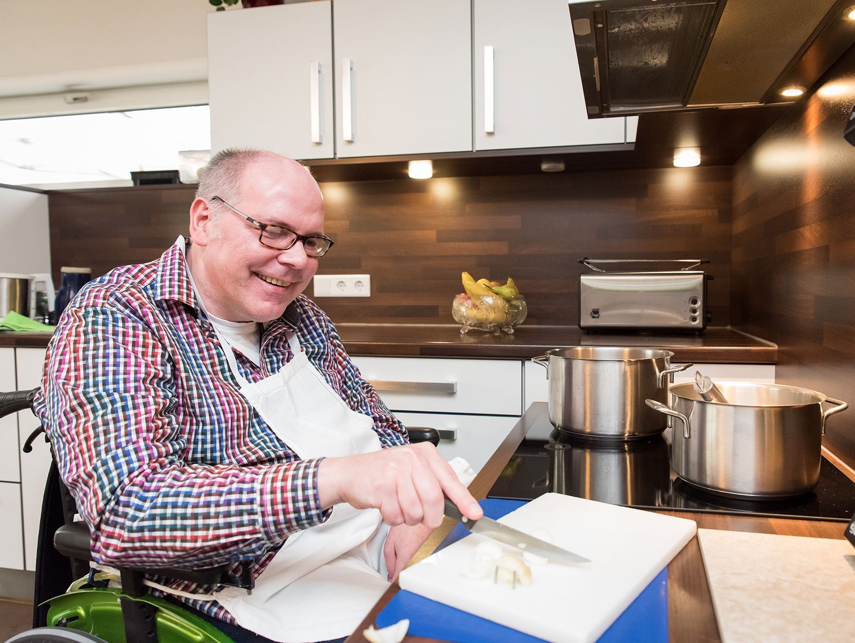 Küchenarbeit: Ein Mann im Rollstuhl schneidet Zwiebeln - lacht dabei