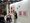 Eine Frau steht vor einer weißen Wand in einer Galerie und spricht mit einer Frau im Rollstuhl. An der Wand hängen ein großes buntes Gemälde und kleinere Drucke in Pinktönen. Links sitzen weitere Besucher, darunter eine weitere Person im Rollstuhl, in der hellen Ausstellungshalle.