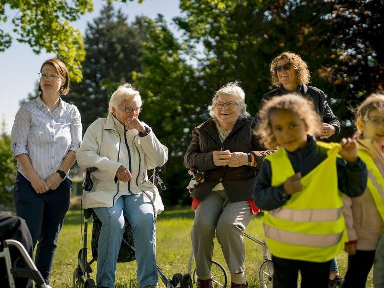 Mitarbeitende, Senioren und Kinder stehen auf einer Wiese und unterhalten sich.