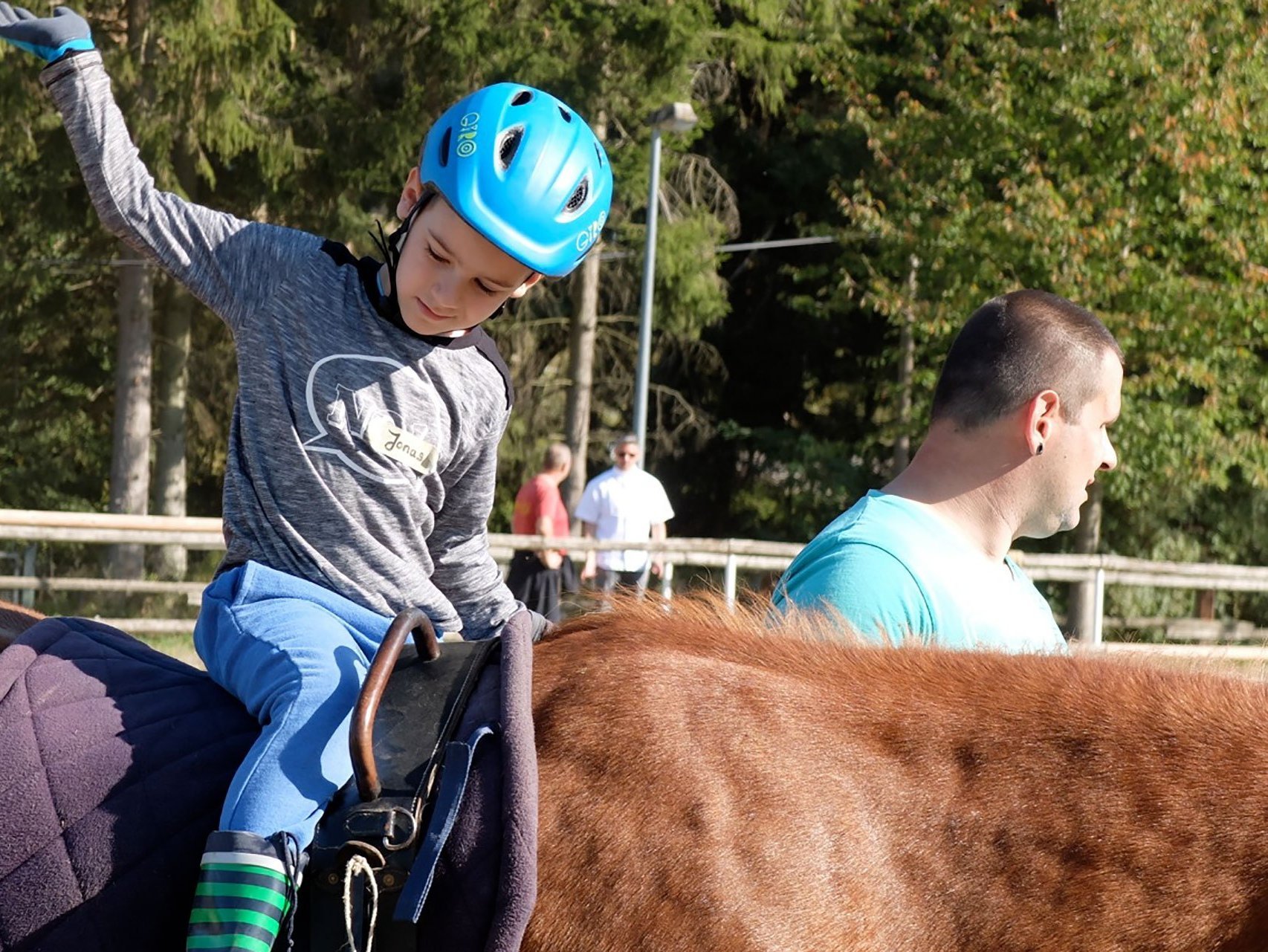 Ein Junge mit Fahrradhelm sitzt auf einem Pferd, das von einem Begleiter geführt wird