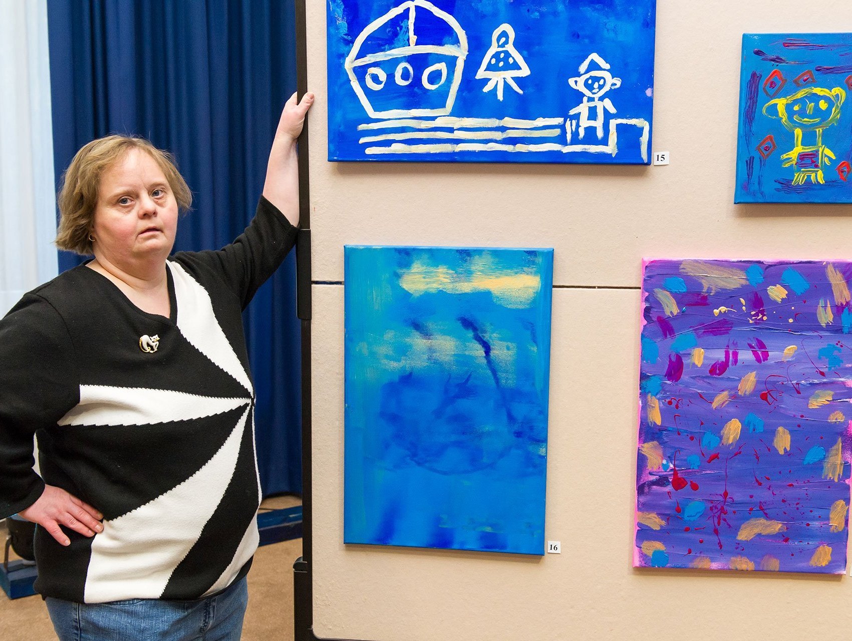 Eine Frau zeigt handgemalte Bilder an einer Wand - alle Bilder sind in blau gehalten