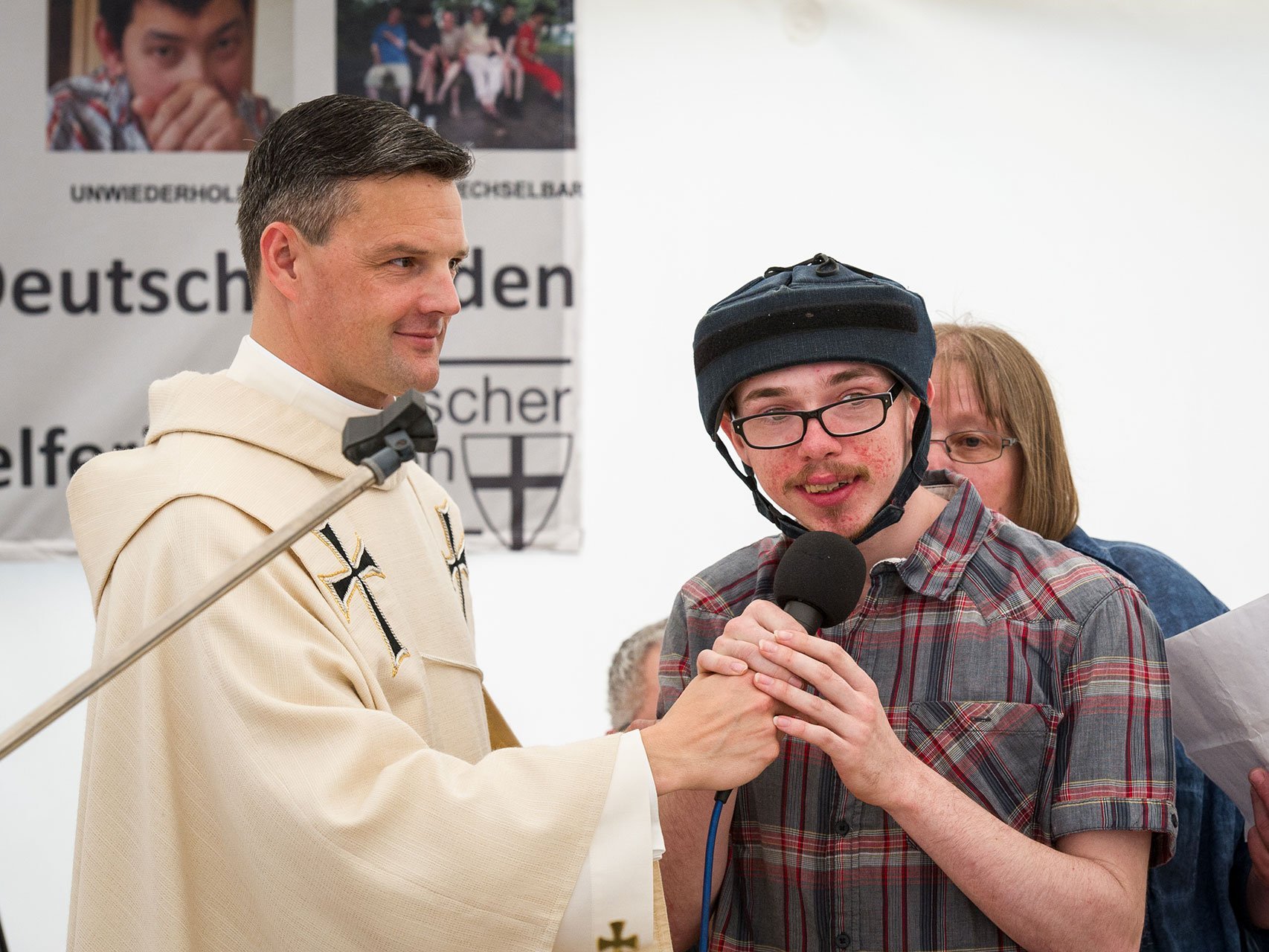 Pater Jörg hält ein Mikrofon für einen jungen Mann mit Kopfschutz, der gerade spricht