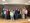 Ein Gruppenfoto von etwa 20 Personen, überwiegend älteren Erwachsenen, die auf einer Holzbühne in einem hellen Raum stehen. Sie tragen alltägliche Freizeitkleidung und blicken freundlich in die Kamera.